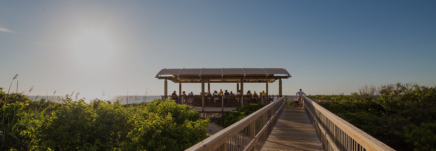 a boardwalk leading to a covered seating area just in front of the beach