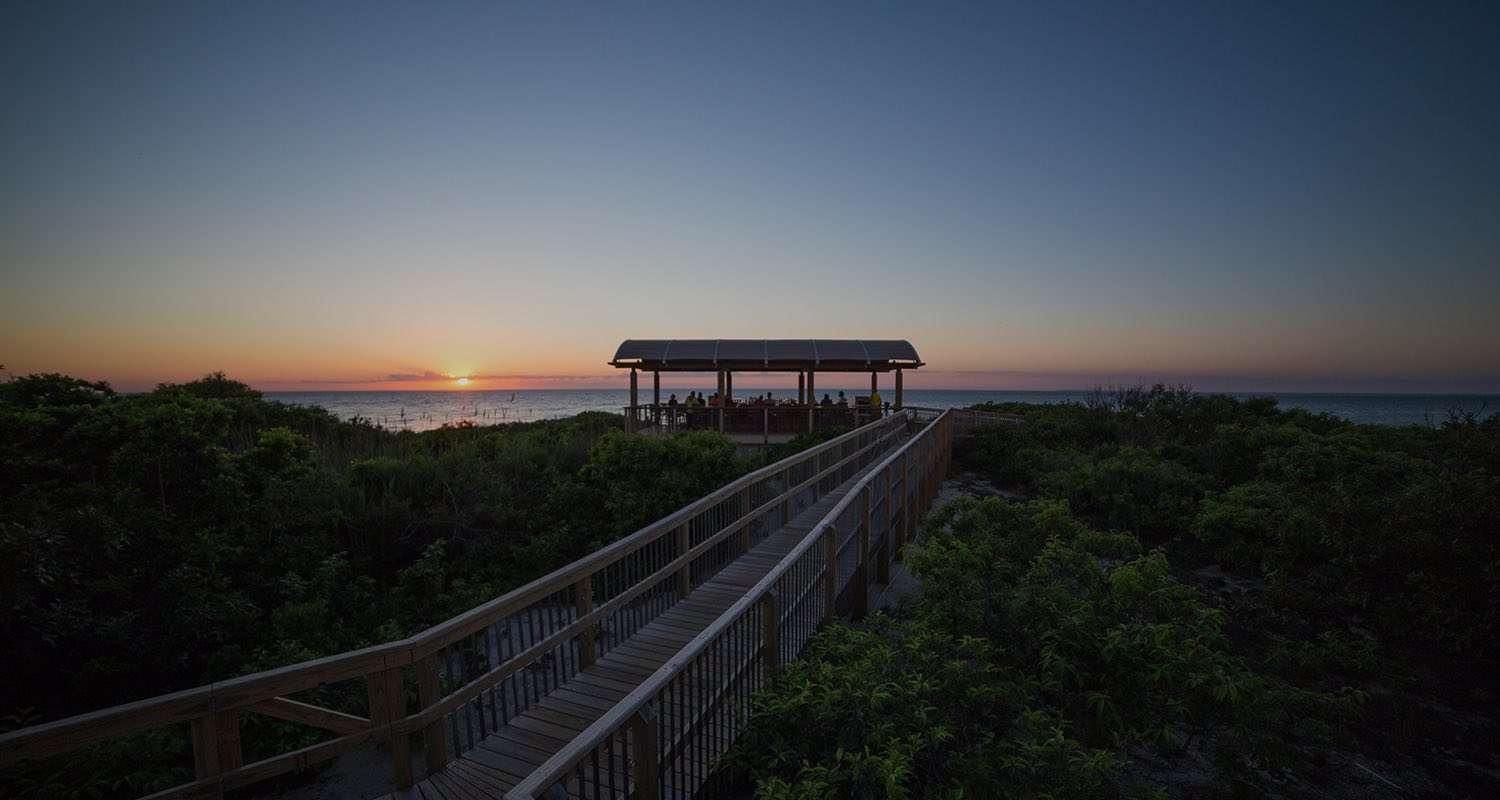 view of a boardwalk with a cabana and sunsetting in the background