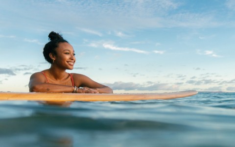 girl resting on her yellow surfboard in the middle of the ocean
