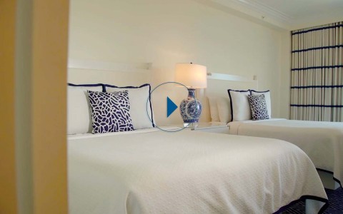 ocean view balcony with 2 queen beds and a white comforter and blue carpet