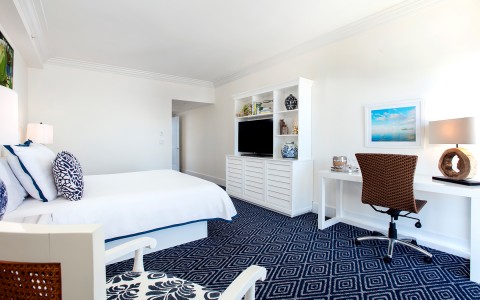 corner view of hotel room with white desk and tv located in white hutch 