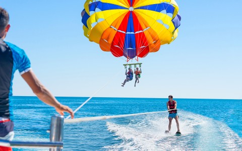 a couple parasailing and a man on water skis 