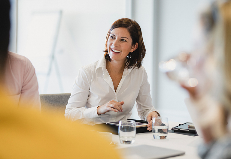View of a woman in a meeting smiling and looking to the left side while she is holding a tablet