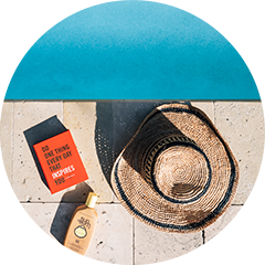 Top view of a beach hat, sunscreen and a book next to the pool