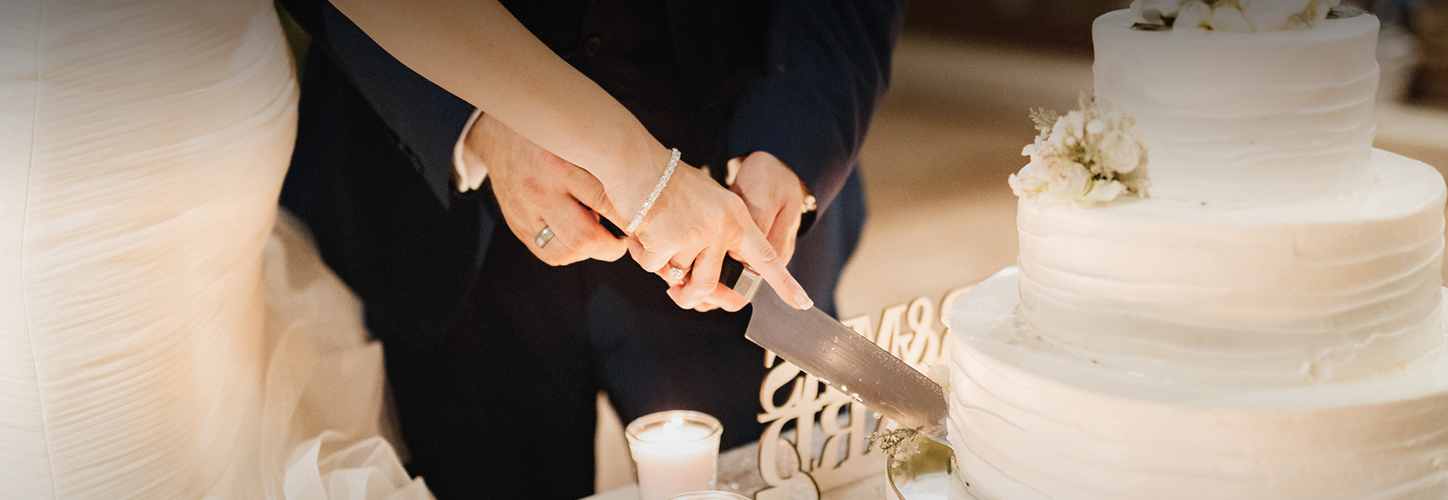 Hands of a bride and groom cutting the cake