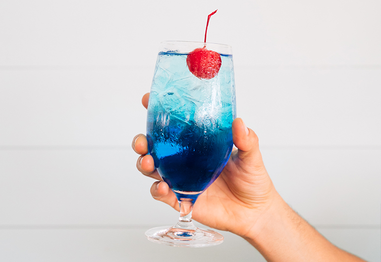 A person holding a tropical blue cocktail 