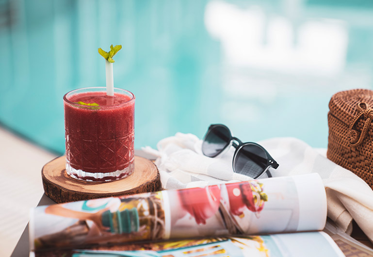 Close up of a tropical beverage, a pair of sun glasses and a magazine all on a wooden table