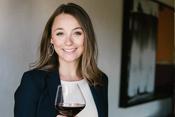 Well dressed woman smiling and holding a glass of red wine looking straight to the camera