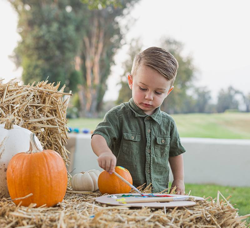 litlte boy painting pumpkin sitting on hay