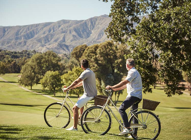 2 men riding bikes through green area