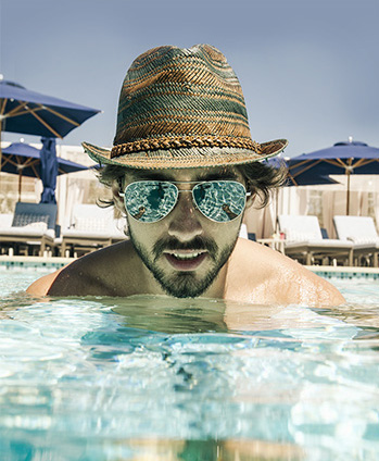 man with fedora and sunglasses shoulder deep in the pool