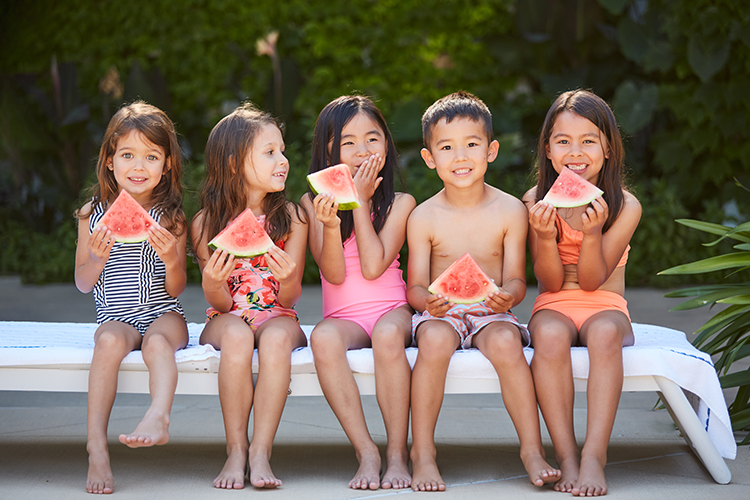 Group of little kids in swim suites eating watermelon