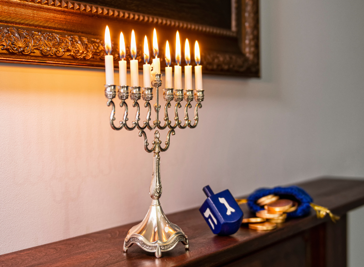 A lit menorah next to a dreidel and some gold coins 