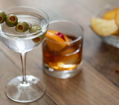 Martini with olives and a glass of scotch with orange slice