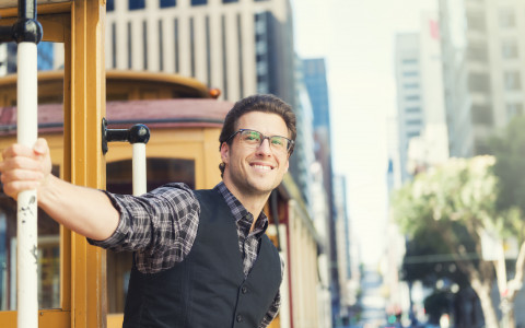 man outside of trolley smiling with glasses