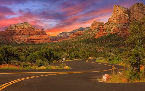 winding road with the mountains in the distance at sunset with a purple and pink sky