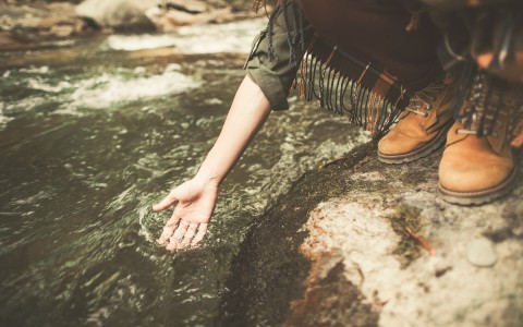 close up of a woman dipping her hand in creek water