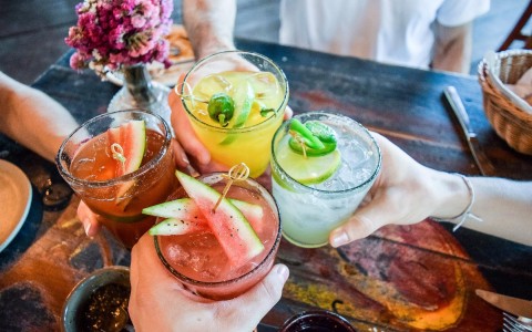 friends holding four fruity cocktail drinks together for a toast