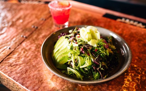 a salad of greens, avocado and a mixed drink topped with fruit