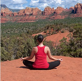woman doing yoga on a red rock overlooking the mountains in the distance