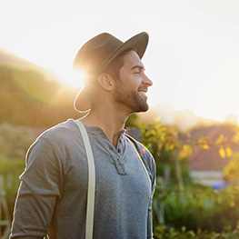 man wearing a hat walking outside with sun gleaming behind him