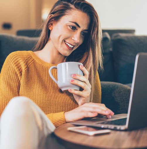 woman sitting at a cozy desk working on her laptop with a cup of coffee