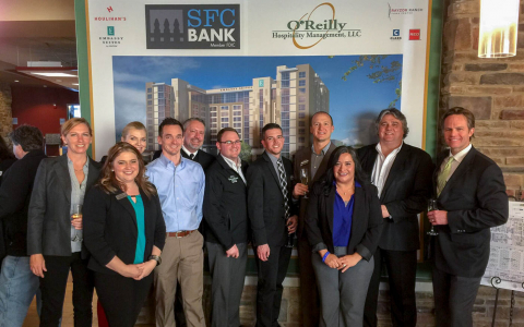 Team members posing in front of Embassy Suites poster