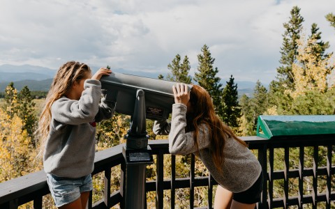 two friends looking through a telescope outside