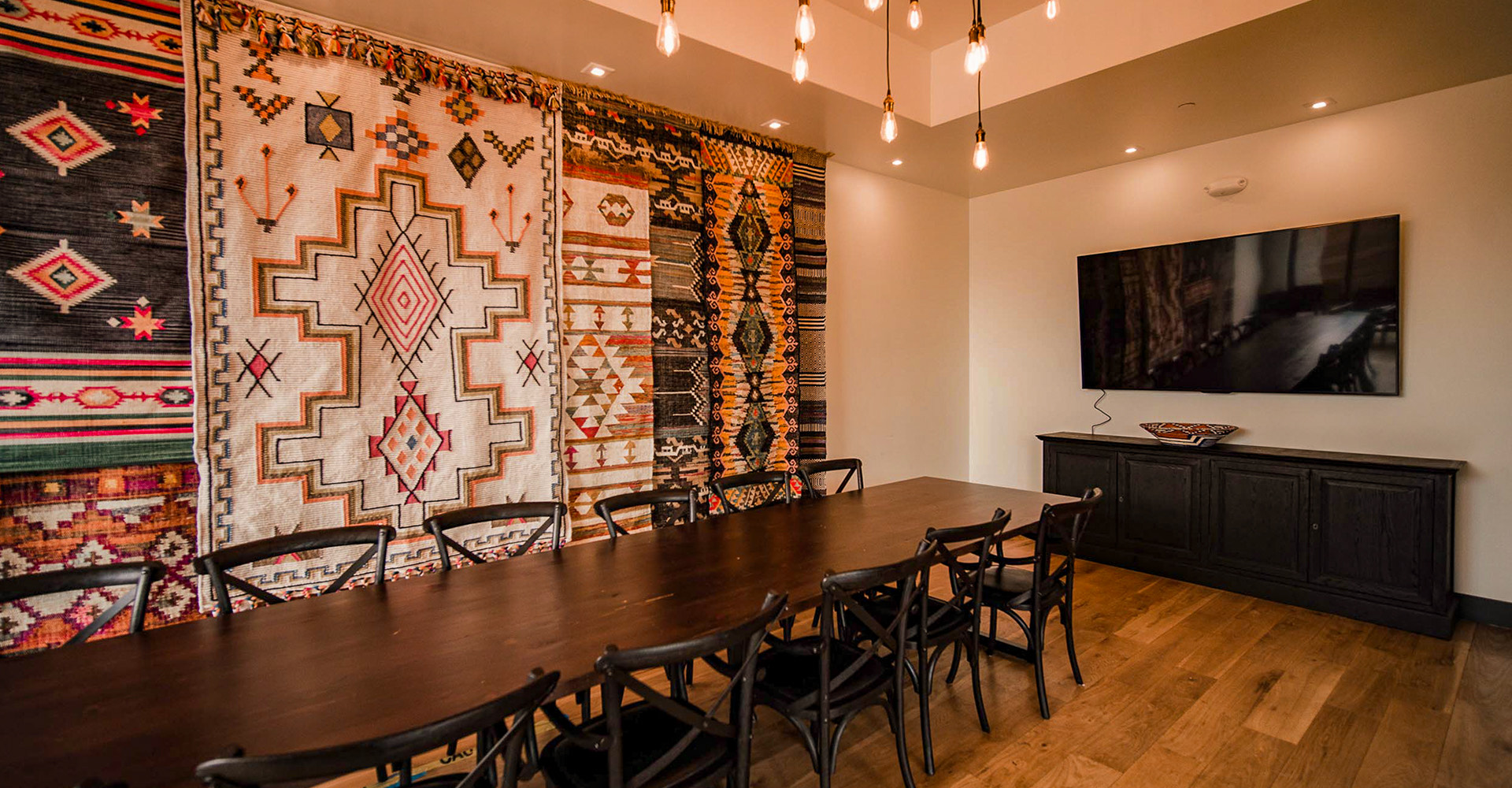 long wooden table in front of a wall with tribal rugs