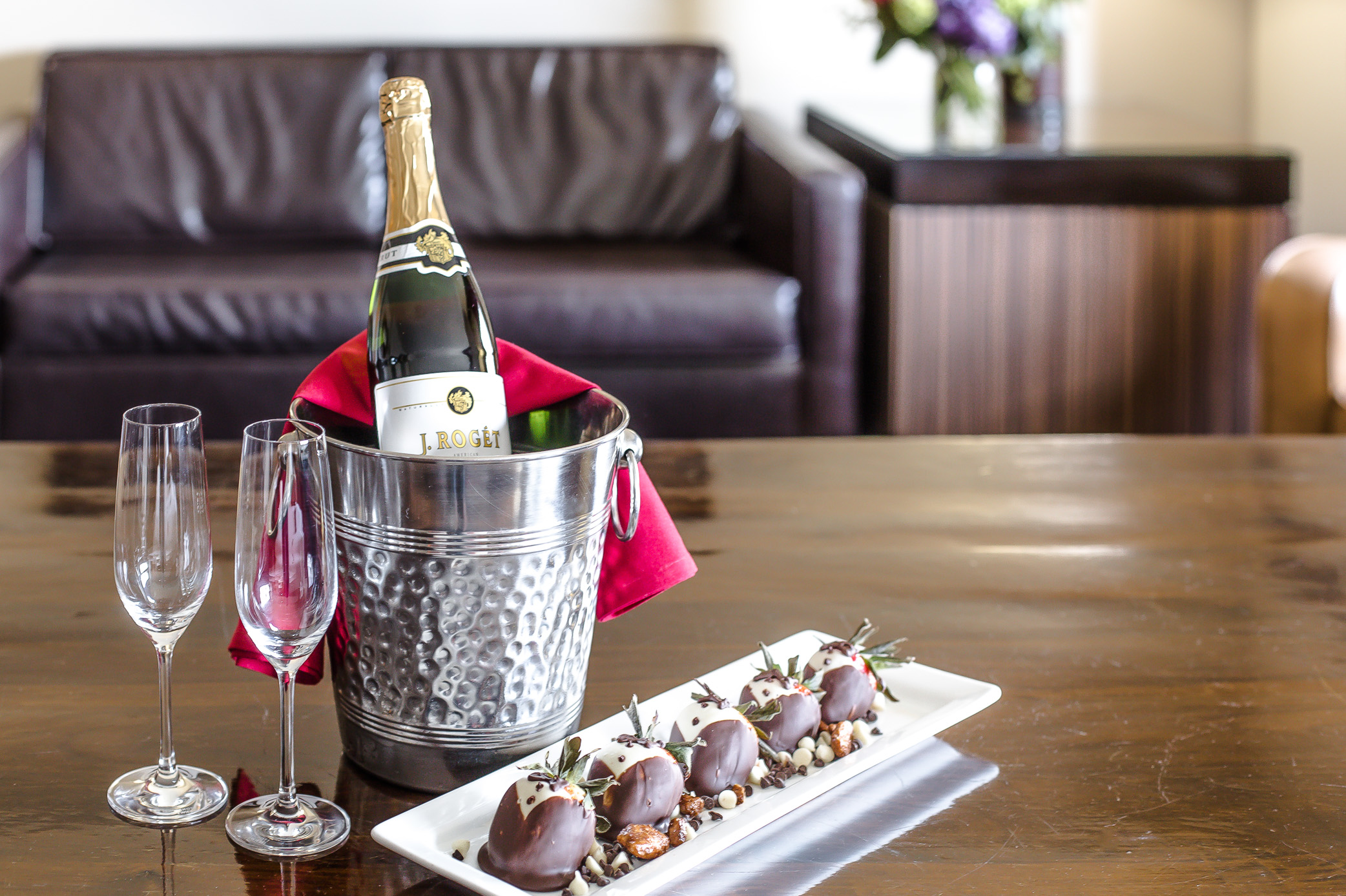a bottle of champagne with two glasses and chocolate covered strawberries on a white plate