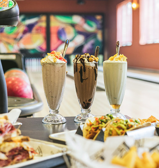 Three different milkshake flavors, taquitos and chips serve in a bowling table
