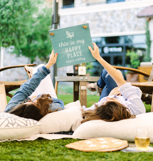 Two women laying down in the grass holding a book
