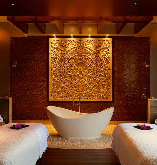 Empty spa room with gold accents, two massage beds and a bath between them