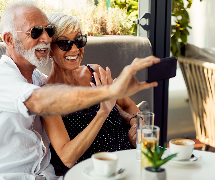 Old couple sitting on a table with coffees on a video call using cellphone