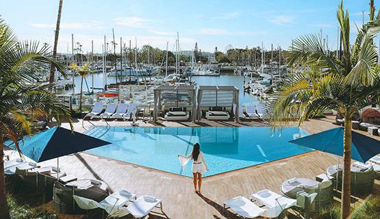 Aerial view of a woman near the pool next to sunbathing chairs with the boats parked in the marina on a sunny day