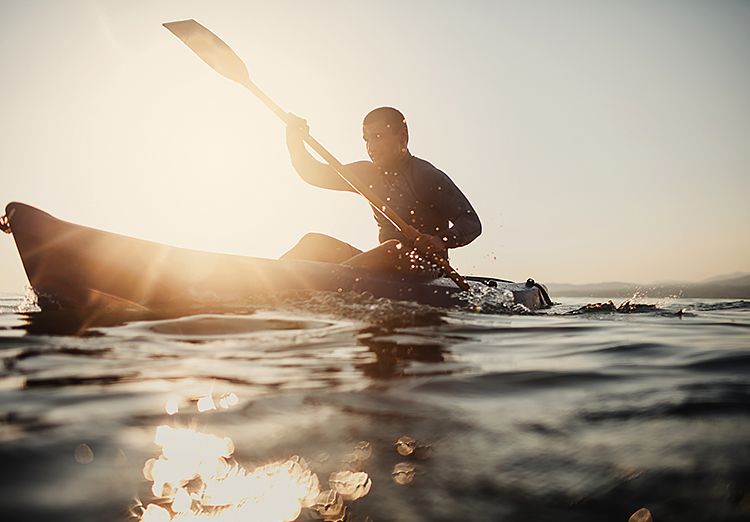 Man kayaking on water with sun setting in the back