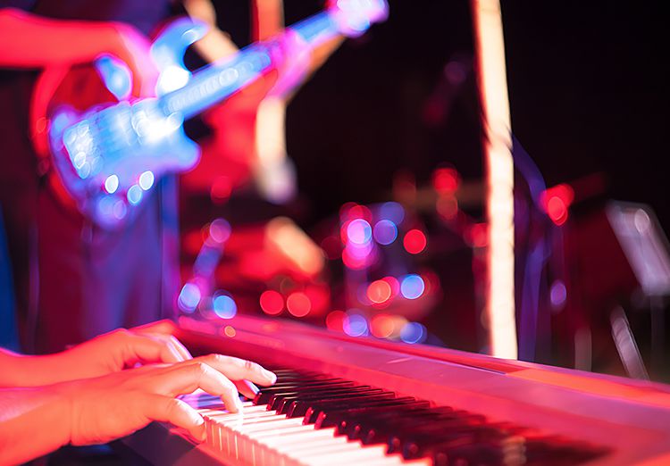 Close up of hands playing piano during concert with guitar player in the back