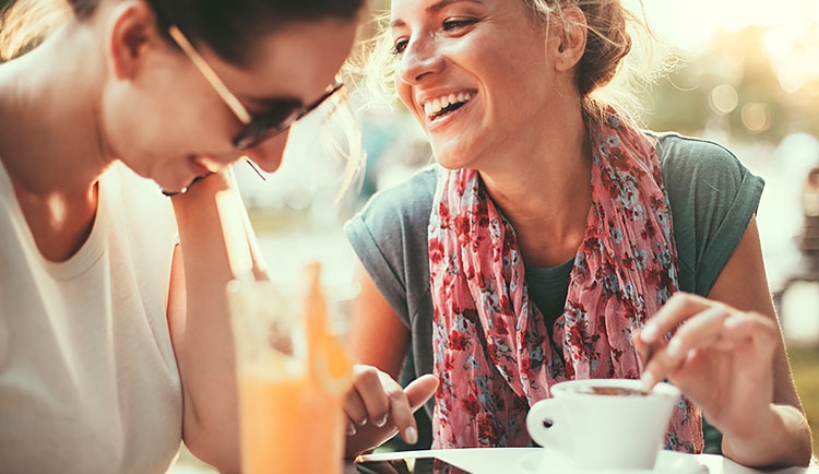 Two women sitting at table outside with juice & coffee