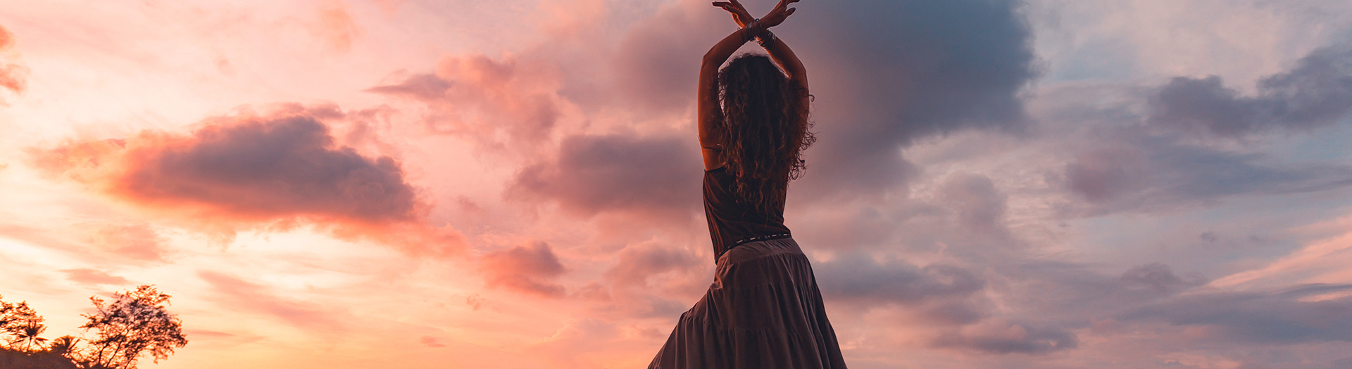 woman standing with arms open in front of the sunset