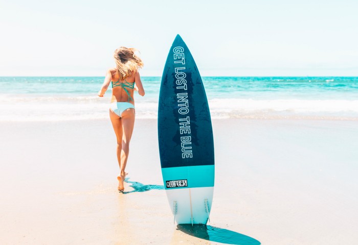 surfboard on the beach with a woman running to the ocean 