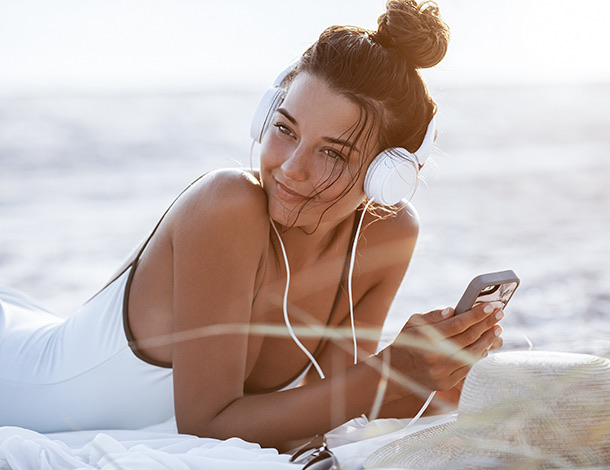 tan woman sitting on the beach with headphoneson