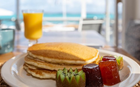 close up view of stack of pancakes with side of fruit and orange juice