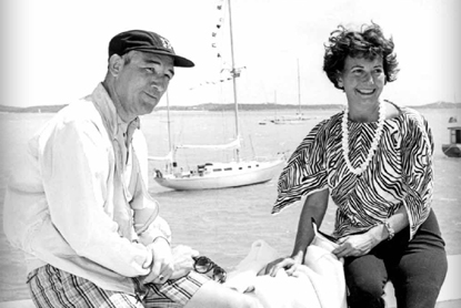 old black and white picture of a couple and a boat behind them