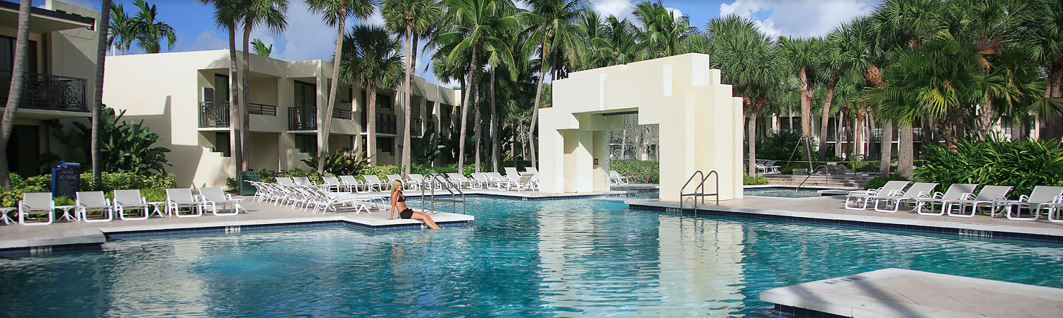 Woman sitting on pool edge surrounded by loungers & palm trees