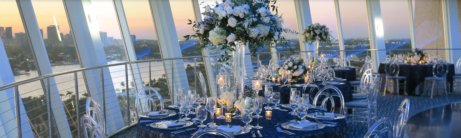 Room set for wedding reception with round tables & large window panels overlooking ocean
