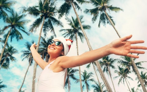female with arms wide open santa hat palm trees behind her 