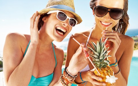 two women laughing drinking out of a pineapple in bathing suits 