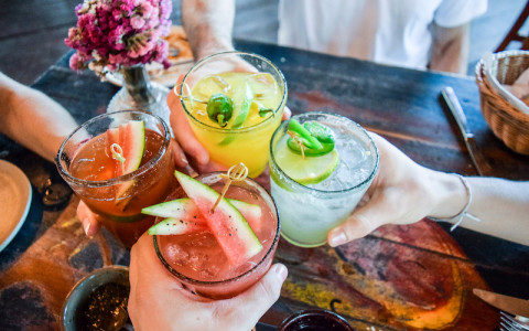 the hands of four people toasting with four different cocktails