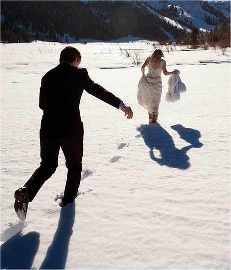 A bride and a groom walking through the snow