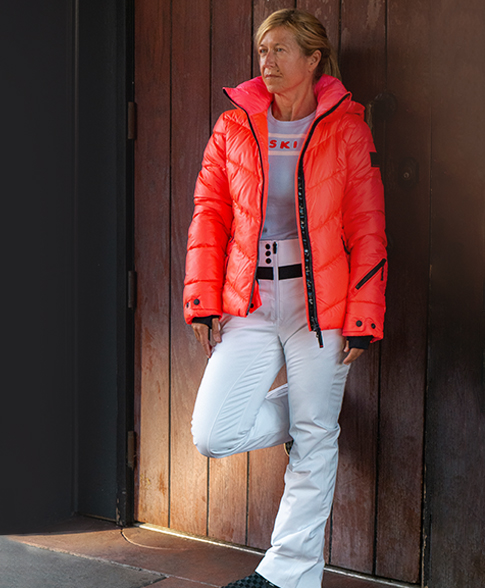 Portrait of a blonde woman wearing a winter salmon jacket and white pants